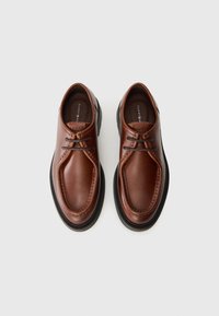 Braune Lederschuhe mit glatter Oberfläche, runder Zehenform und dekorativen Nähten. Sie verfügen über ein Schnürdesign und eine kontrastierende schwarze Gummisohle.