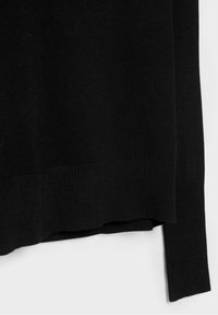 Ourlet et manches d'un pull noir en tricot avec poignets côtelés sur fond blanc.