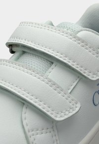 Λευκό αθλητικό παπούτσι με δύο λουράκια Velcro, λείο συνθετικό υλικό, ανοιχτό μπλε διακοσμητικά στοιχεία, υφή υφάσματος κοντά στον αστράγαλο και αντίθετη ραφή.