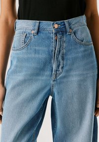 Jeans de mezclilla azul claro con cintura alta, diseño de cinco bolsillos, cierre con botón de cobre y sutiles desgastes, con corte de pierna recta.