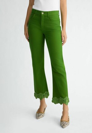 Jean en denim vert avec une coupe évasée et une finition en dentelle au bas. Équipé d'une fermeture à bouton et à zip à l'avant, de cinq poches et de passants de ceinture.