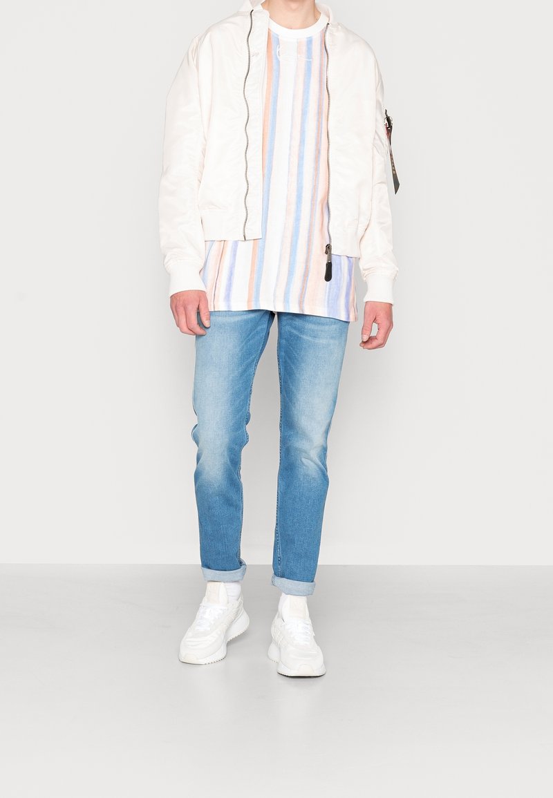 Biała kurtka typu bomber, wielokolorowa koszula w paski, jasnoniebieskie dżinsy i białe trampki. Casualowy strój o luźnym kroju i miękkich fakturach.