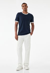 Marineblå kortærmet t-shirt med hvid ribkant ved halsen og ærmekanterne, parret med off-white cargo-bukser med sidelommer og en afslappet pasform.