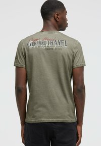 Olive green cotton t-shirt featuring short sleeves, crew neck, and a printed graphic text on the back with faded accents.