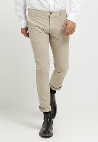 Béžové chinos s úzkým střihem, s jedním černým knoflíkem a poutky na pás, doplněné černými kotníkovými botami; hladký bavlněný materiál.