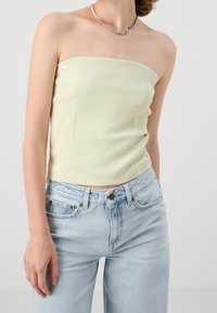 Top sans bretelles jaune clair avec un design ajusté et une texture lisse, associé à un jean en denim bleu clair taille haute. Accent collier en argent.