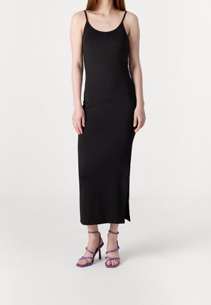 Black, sleeveless, maxi dress with a fitted design and side slit; paired with purple strappy high-heeled sandals.