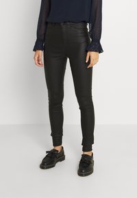 Black faux leather skinny pants with a high waist, smooth texture, and ankle-length. Paired with black flat shoes and a navy long-sleeve top.