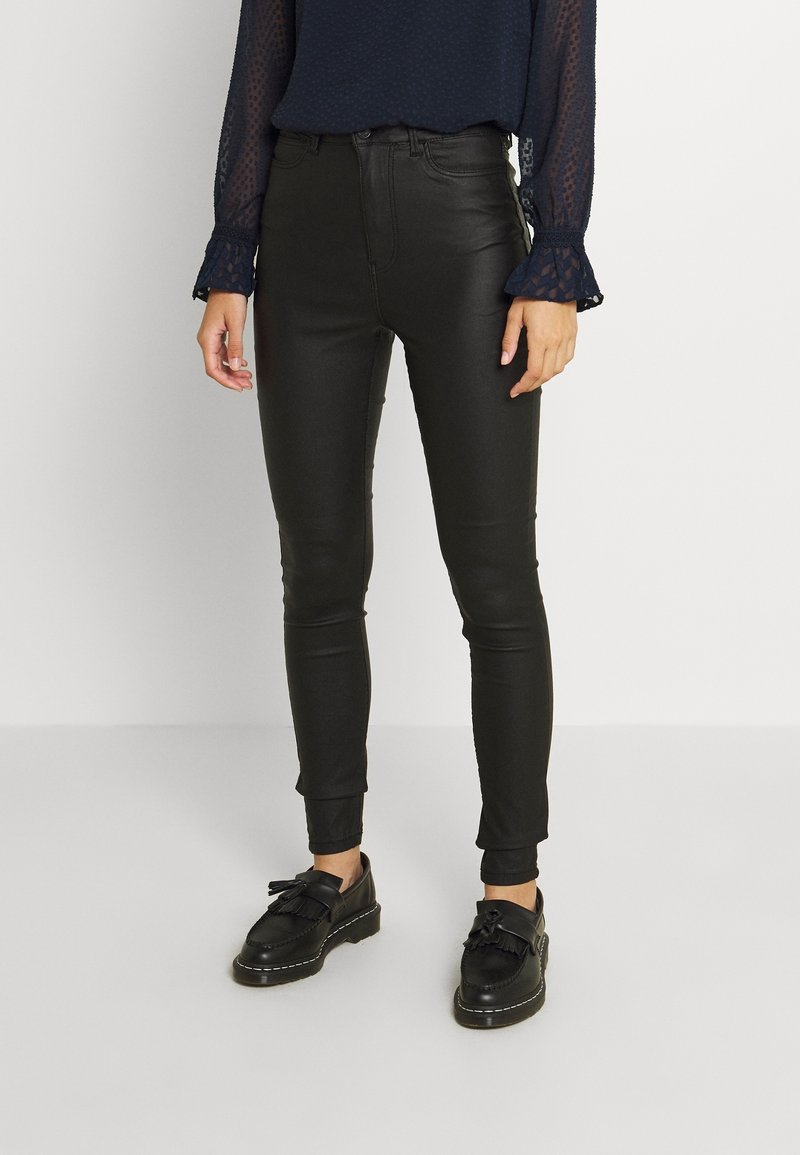 Black faux leather skinny pants with a high waist, smooth texture, and ankle-length. Paired with black flat shoes and a navy long-sleeve top.