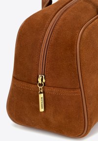 Borsa in suede marrone con forma arrotondata, dettagli con zip dorata e un accento in pelle attorno all'apertura. Etichetta con logo attaccata alla zip.