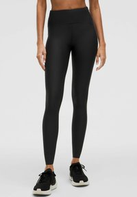 Leggings negros de cintura alta con una textura suave, que presentan un sutil patrón diagonal y un diseño ajustado, combinados con zapatillas deportivas negras.