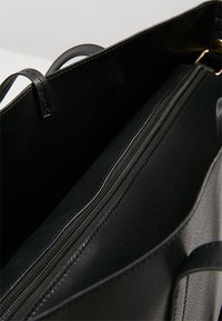 Intérieur d'un sac fourre-tout en cuir noir, avec une texture lisse, un compartiment zippé et un dessus ouvert avec des poignées doubles.