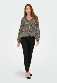 Blusa con stampa zebras in nero e beige, con scollatura a V e maniche lunghe, abbinata a jeans skinny neri e ballerine nere.