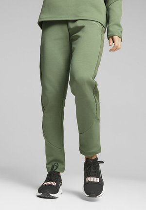 Pantalones deportivos verdes con un acabado texturizado, que presentan paneles laterales de malla y un diseño ajustado, combinados con zapatillas negras que muestran la marca "PUMA".