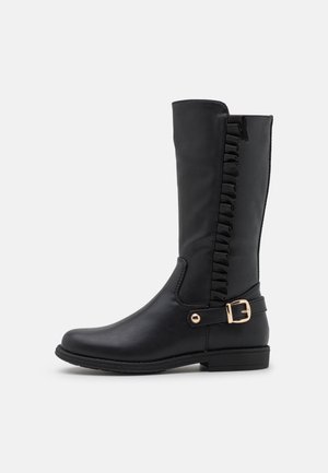 Botte noire mi-mollet avec bordure à volants sur le côté et une bride à boucle dorée près de la cheville, semelle plate avec un léger talon.