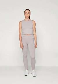 Lys grå treningssett som består av en ermeløs crop top og høyhåret leggings. Glatt tekstur med minimal merkevare og atletiske sneakers.