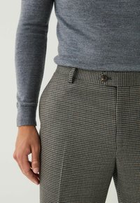 Gray knit sweater paired with check-patterned trousers in brown and beige, featuring a button closure and side pockets.