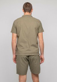 Chemise olive à manches courtes avec un ourlet droit et un col, assortie à un short. Tissu léger ; coutures minimales visibles.