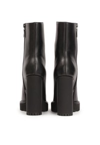 Paire de bottines en cuir noir avec talons hauts épais et fermetures éclair à l'arrière, vues de dos sur fond blanc.