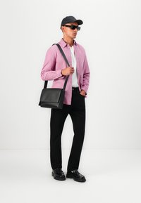 Sac messager noir, chemise rose à boutons, sous-vêtement blanc, pantalon noir et chaussures noires. Les accessoires comprennent une casquette noire et des lunettes de soleil.