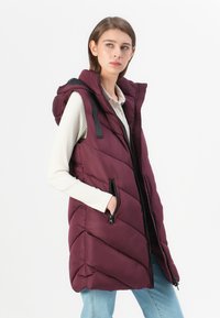 Gilet sans manches matelassé en bordeaux profond avec un motif matelassé en diagonale, fermeture éclair frontale, poches latérales et capuche ajustable. Texture du tissu douce.