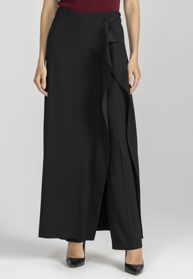 Czarna spódnica kopertowa z lekkiego, lejącego się materiału, z wiązaniem po boku i warstwowym fasonem. Długość sięga do kostek, a tkanina ma gładką fakturę.