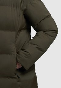 Puffermantel in dunkelolivgrün, mit gesteppten Abschnitten, einem erhöhten Kragen und einer Seitentasche mit Kordelzugverschluss.
