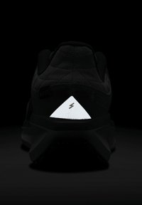 Chaussure de sport noire avec un dessus matelassé, semelle en caoutchouc et détail triangulaire réfléchissant blanc au niveau du talon, arborant un symbole d'éclair.