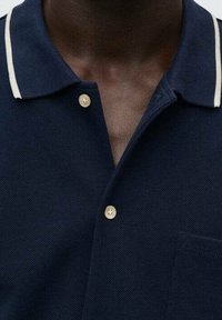 Polo shirt blu navy realizzato in tessuto testurizzato, con colletto classico, una tasca singola, strisce bianche a contrasto e chiusura con bottone dorato.