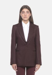 Blazer bordeaux a righe sottili con chiusura a un bottone, rever a isolino e tasche frontali, indossato sopra una camicia bianca con colletto.