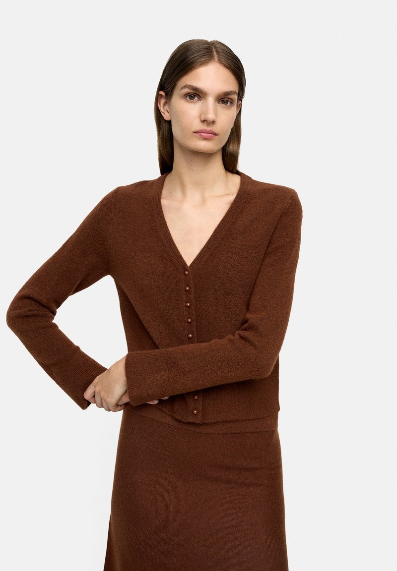 Brązowy, teksturowany kardigan z dzianiny z dekoltem w kształcie litery V i zapięciem na guziki z przodu, w zestawie z dopasowaną spódnicą.