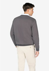 Grijze sweatshirt met een ribbelboord en manchetten, met daaronder een witte kraag. Draag het met lichtbeige broek, die minimale details op de stof toont.