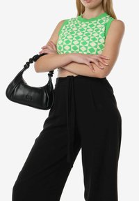 Groen gebreide top met geometrisch patroon, gecombineerd met zwarte hoog-getailleerde broek. Zwarte leren handtas met gedraaide handgreep.