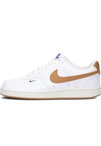 Zapatilla blanca con una parte superior de cuero texturizado, swoosh de cuero marrón y logo azul. Presenta perforaciones en la puntera y una suela de goma.