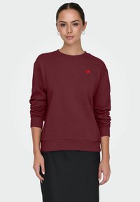 Bordeaux sweatshirt met een ronde hals, ribgebreide manchetten en zoom; heeft een klein rood hartembleem op de borst. Glad stofoppervlak.