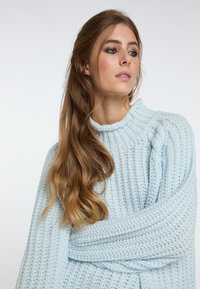 Light blue knitted sweater with a high neck, ribbed texture, and oversized fit, featuring long sleeves and a soft, cozy appearance.