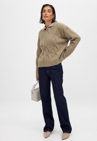 Beige kabelstickad tröja med V-ringning, kombinerad med mörkblå vida jeans. Accessoarer inkluderar en ljusgrå handväska och spetsiga beige klackar.