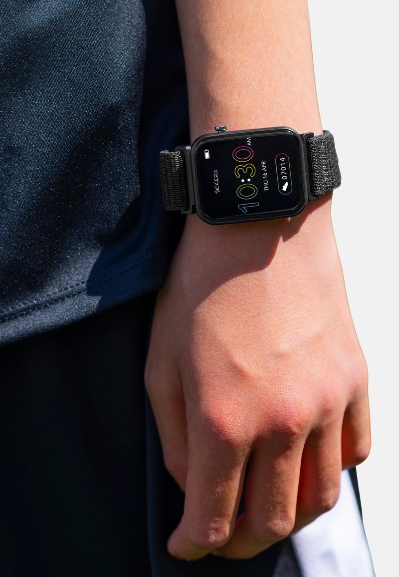 Pols met zwart fitness smartwatche die tijd, datum, batterijstatus en stappenteller weergeeft, gedragen over donkere kleding.