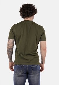 T-shirt verde oliva a maniche corte, in tessuto misto cotone, colletto tondo, texture liscia, indossato con jeans blu in denim, vista posteriore.