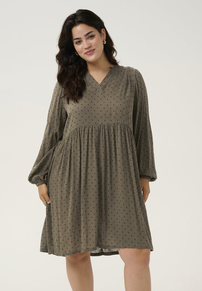 Robe vert olive avec de longues manches bouffantes, décolleté en V, et une jupe évasée, ornée de pois noirs et d'un tissu texturé.