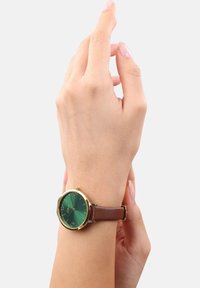 Braunes Lederarmbanduhr mit grünem Ziffernblatt, goldfarbenem Gehäuse und silbernen Akzenten. Zahlen an den Positionen 12, 3, 6 und 9 auf dem Ziffernblatt.