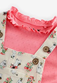 Virágmintás kordbársony kantáros nadrág Moomin illusztrációkkal, fa gombokkal, és alatta egy rózsaszín, texturált fodros felső.