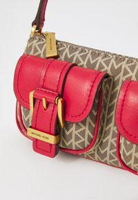 Petite sac à main avec des accents en cuir rouge, des détails en or, et un tissu à motif présentant un design géométrique beige et marron.