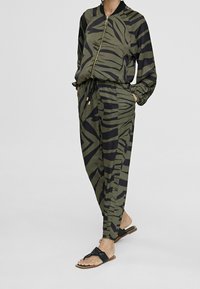 Souprava athleisure skládající se z zelené bomber jacket a odpovídajících tapered kalhot, které mají výrazný černý vzor tygří pruh.