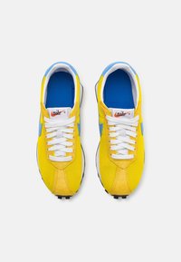 Geltoni tinkliniai ir zomšiniai sportbačiai su mėlynais akcentais, baltais raišteliais, paminkštinimu ir juodais padais. Nike logotipas ant liežuvėlio, elegantiškas dizainas.