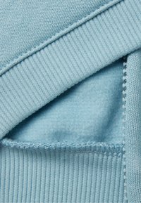 Maglione azzurro chiaro in un tessuto che mostra una morbida trama interna, orlo a costine e dettagli di cucitura a contrasto lungo il bordo.
