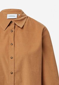 Camicia in corduroy marrone con colletto classico, chiusura a bottoni frontale e sottile texture a coste. Etichetta del marchio visibile sul colletto.
