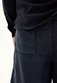 Pantaloni in lino blu navy con tasca posteriore. Il tessuto ha un aspetto texturizzato e leggermente stropicciato, che valorizza il design informale.