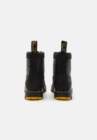 Botine negre la glezna cu un finisaj din piele netedă, accente galbene pe talpă și bucle pentru a fi ușor de încălțat. Părți texturate și design robust.