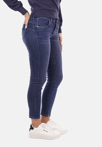 Jeans in denim skinny di color blu scuro, con cinque tasche, dettagli cuciti e vita media. Abbinati a sneakers bianche.